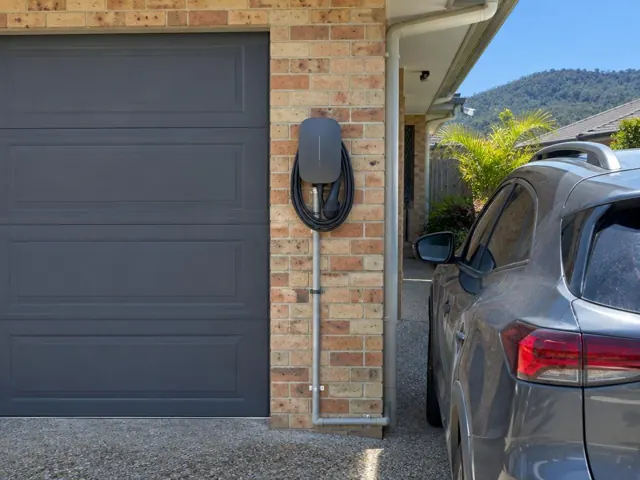 Wall-mounted EV charger on a brick exterior beside a garage and driveway in Upper Coomera